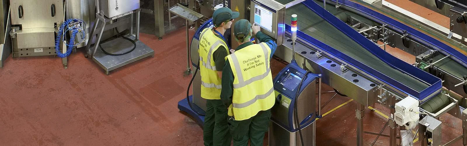 two employees in high vis gathered around domino screen above production line