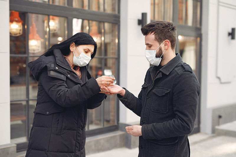 Deux personnes portant un masque facial et utilisant un désinfectant pour les mains