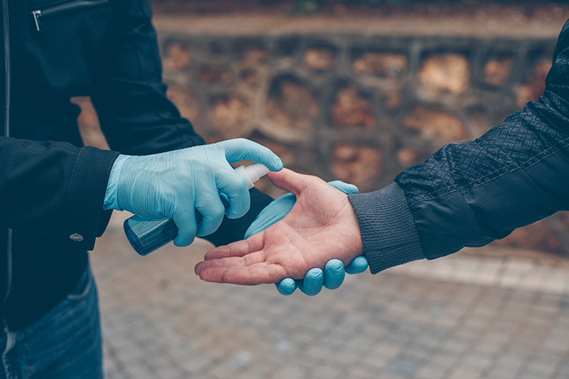 A person wearing blue gloves spraying hand sanitizer 