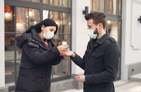 Two people wearing face masks using hand sanitizer