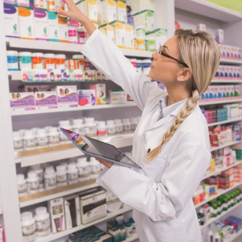 Woman in lab coat in pharmacy picking stock off a shelf 