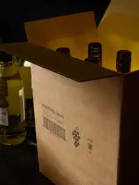 A group of wine bottles inside a porous cardboard box with a Cx150i code printed on the outside.